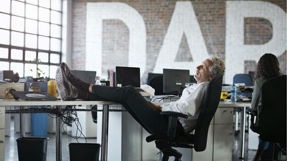 A businessman sleeps in his office chair with his feet on his desk.