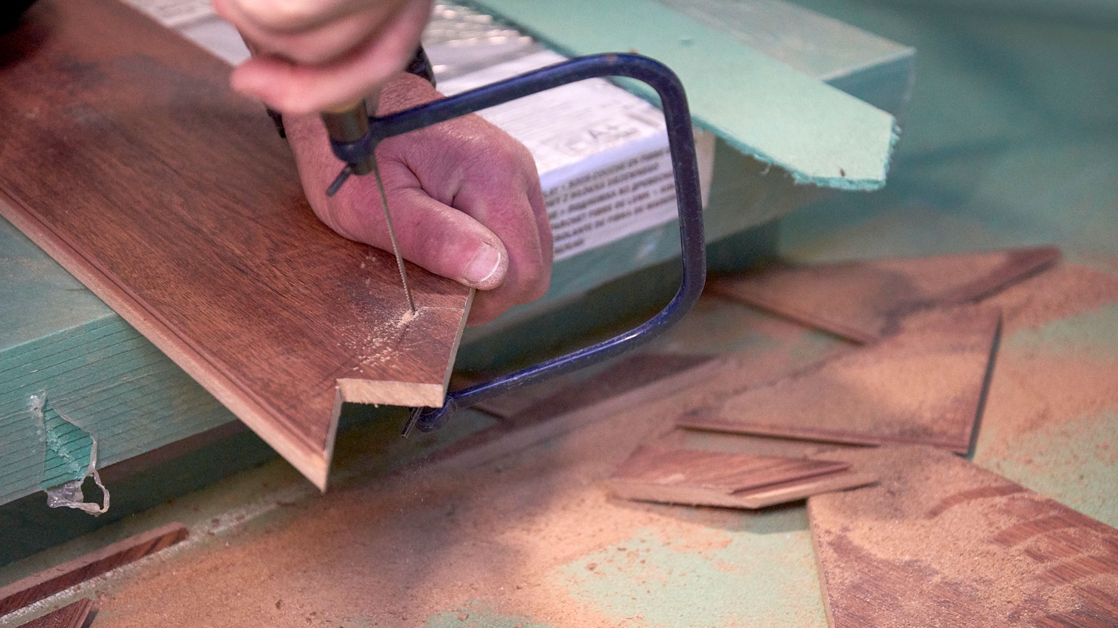 Hand using a coping saw to cut wooden flooring plank