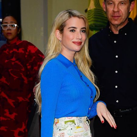Emma Roberts wearing a blue cardigan, canvas print knee-length skirt, yellow handbag, and silver flats