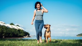 Happy young woman walking her dog on grass near the water