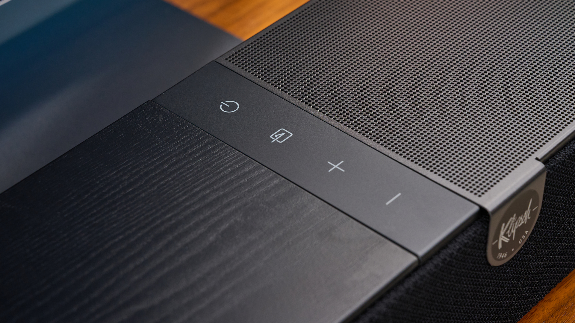 the klipsch flexus core 100 soundbar photographed on a wooden tv stand with a tv behind, showing the remote, buttons, and inputs