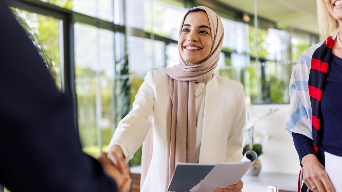 A woman wearing a niqab shakes the hand of a person just out of frame while holding a notebook in her other hand