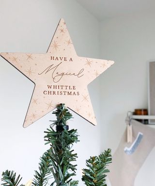 A wooden personalizable Christmas tree topper on top of artificial tree
