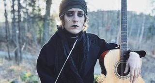 Jonathan Hult&eacute;n wears white makeup and black lipstick and eye-liner and is photographed in the woods with an Ibanez acoustic electric guitar