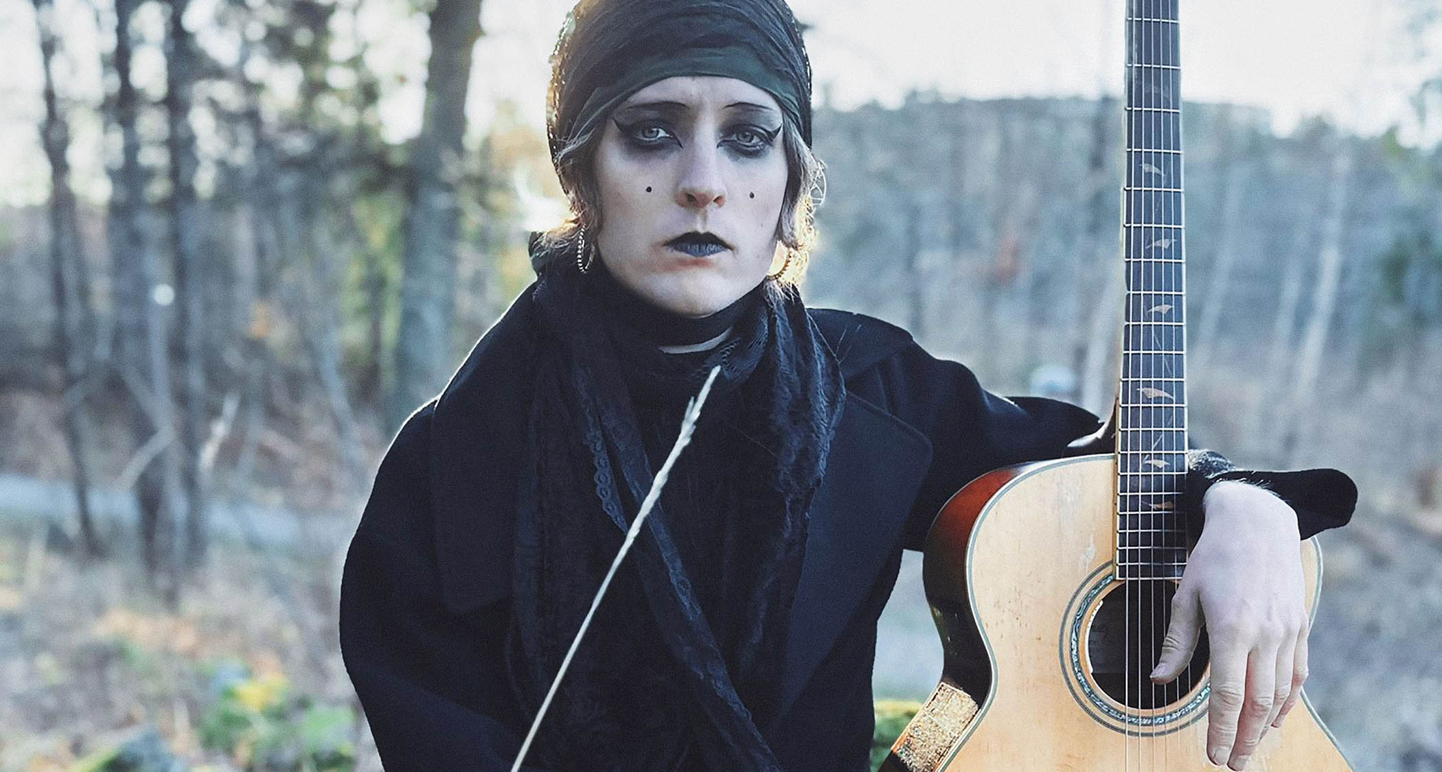 Jonathan Hultén wears white makeup and black lipstick and eye-liner and is photographed in the woods with an Ibanez acoustic electric guitar
