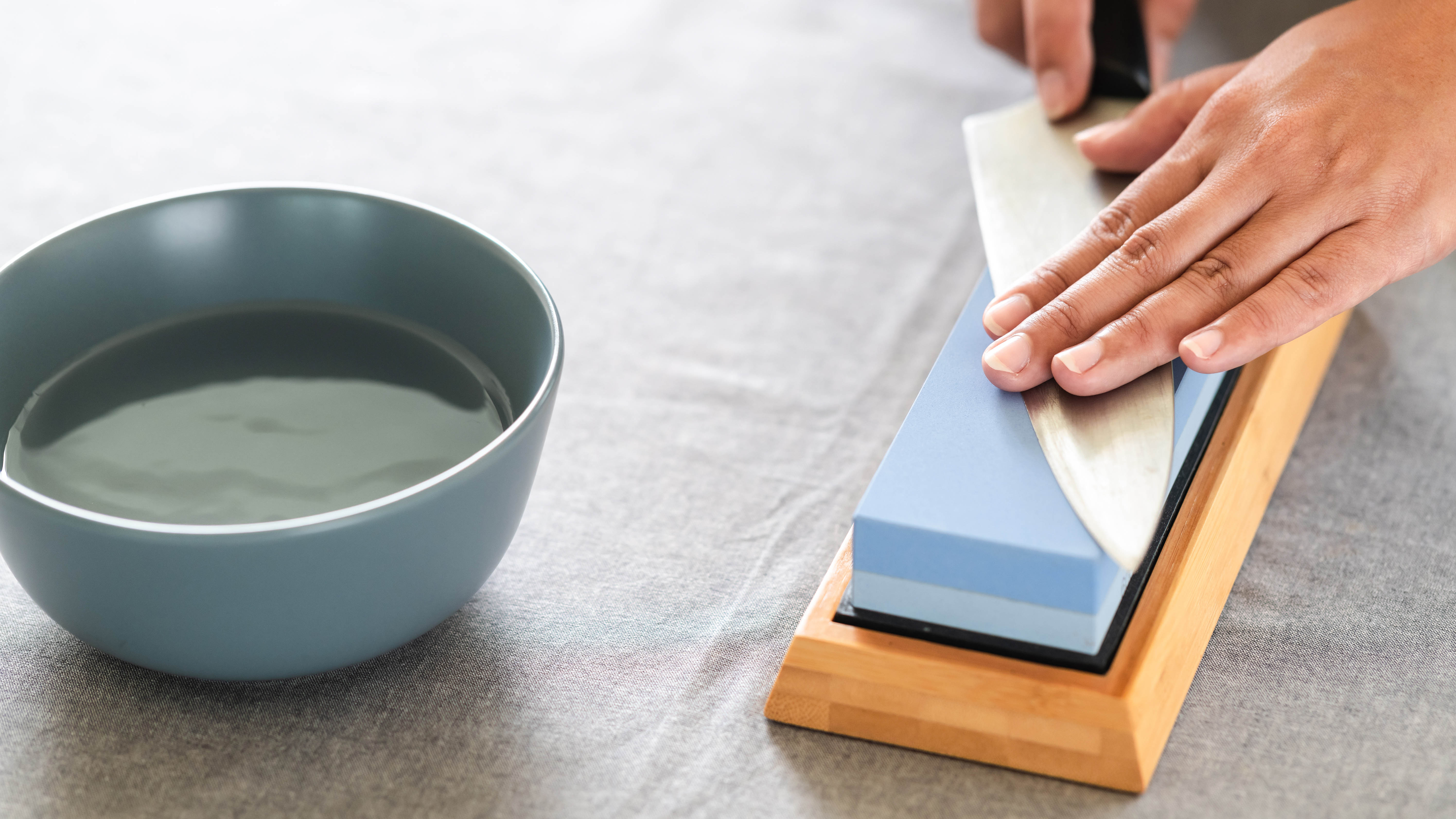 A knife sharpening on a whetstone next to a bowl of water