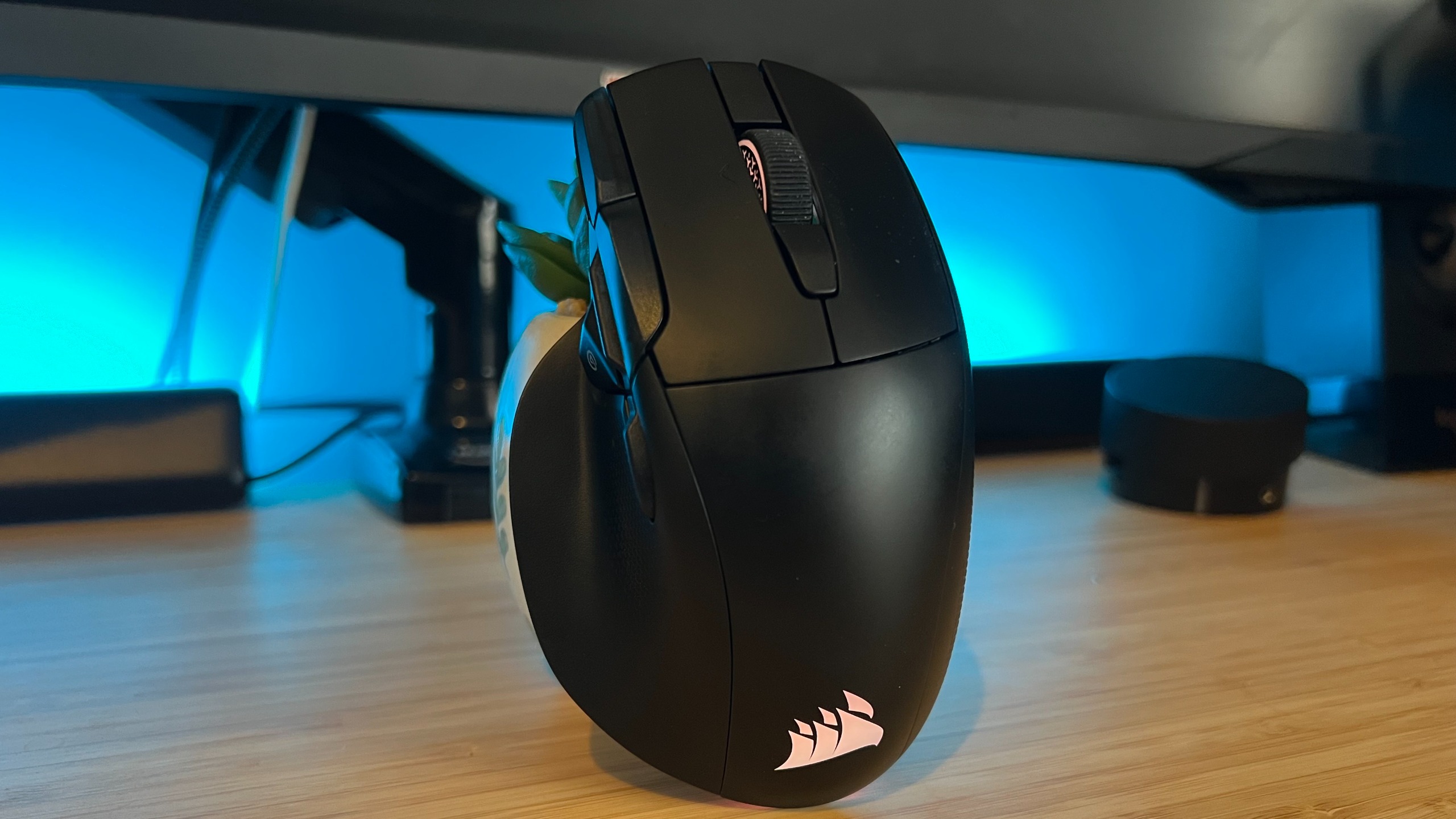 Corsair Nightsword V2 Wireless gaming mouse standing upright on a wooden desk with blue backlighting