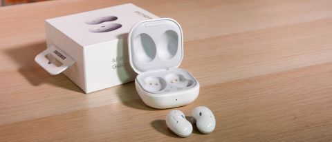 The Samsung Galaxy Buds Live earbuds in white pictured on a wooden surface next to their charging case.