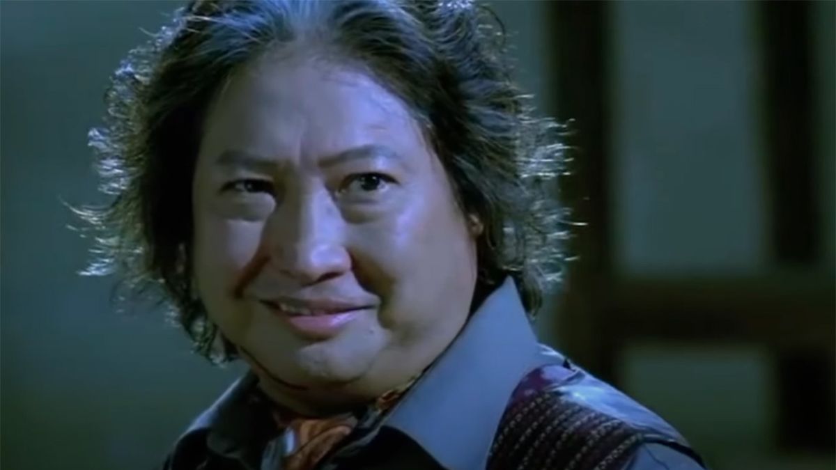 Sammo Hung in a fight scene in a suit and tie in a warehouse.