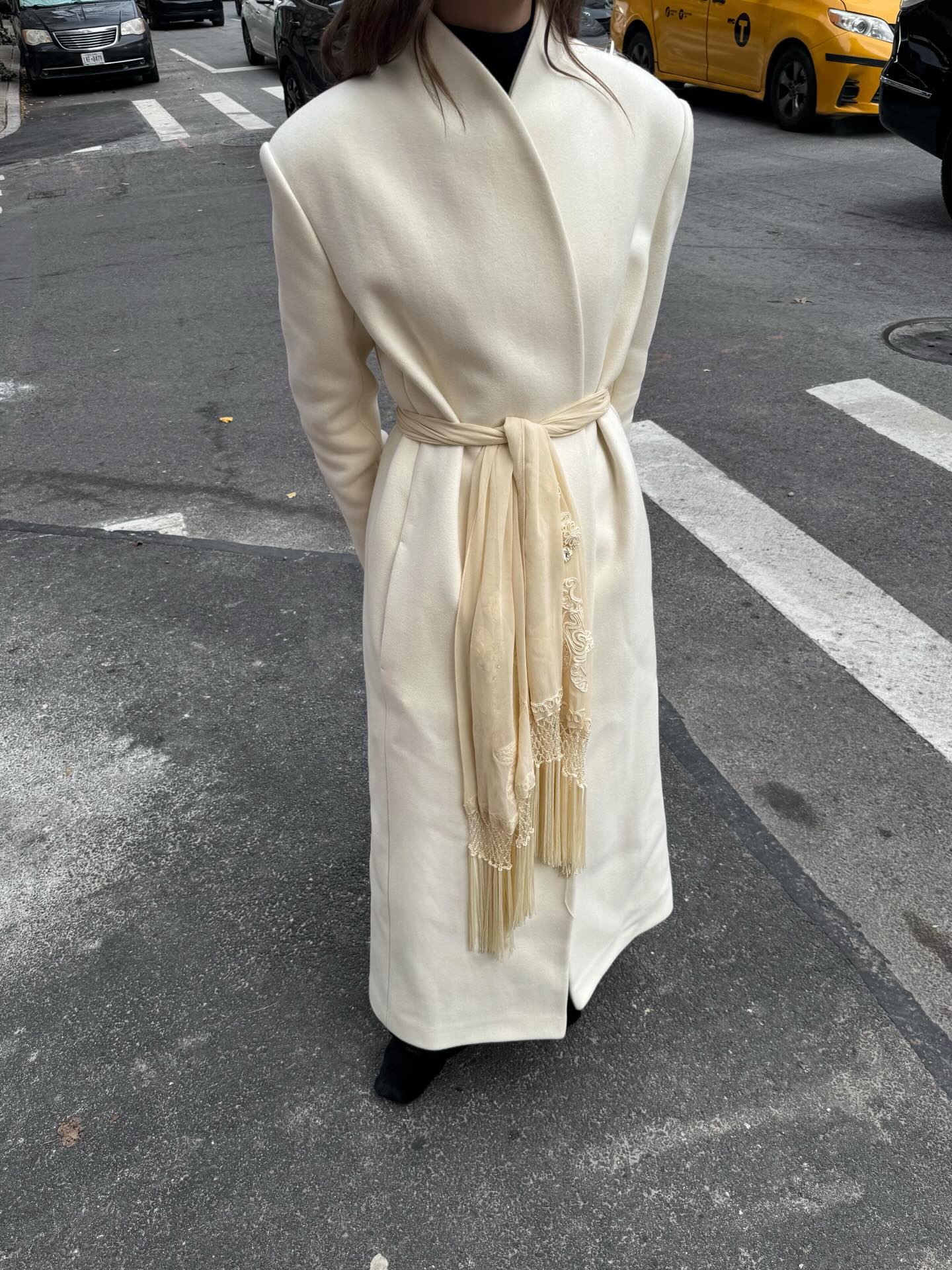 @christietyler wearing a cream coat with a matching fringe scarf tied around her waist.