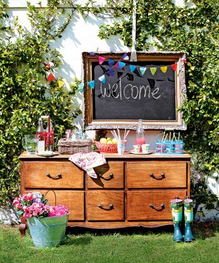 A vintage set of dresser drawers used as a welcome table with a blackboard and drinks