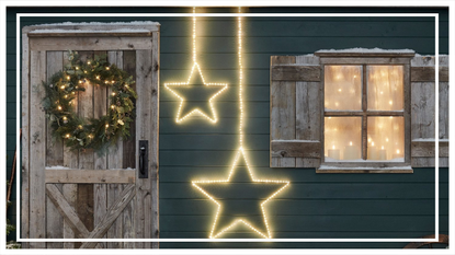 Two star decorations hanging on the front of a Scandinavian-style house, one of the best Christmas lights for 2021