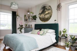 Bedroom with pale pink and green walls, green velvet headboard, spotty white and black bedding and botanical artwork