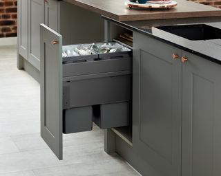 A gray kitchen cupboard that features an integrated trash can, demonstrating kitchen cupboard storage ideas.