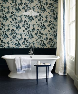 A white roll top bath in a dark bathroom with floral wallpaper