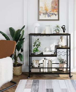 A black bar cart in living room with plant, vase, lampshade and assortment of homeware decor