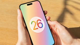 A render of the Apple iOS 26 logo on an iPhone held in a hand.