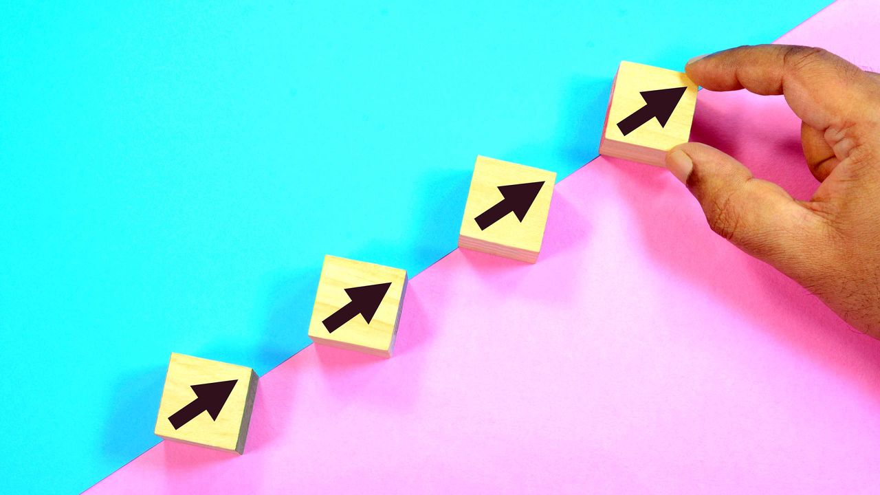 person putting wooden blocks with black arrows in a line dividing pink and blue backdrop