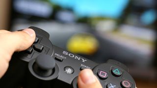 Man's hand holding Sony Dualshock wireless controller while playing Gran Turismo 5 on PlayStation 3.