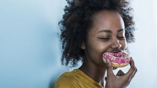 Person enjoying an iced ring doughnut with their eyes closed