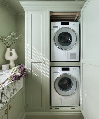 Miele washing machine in a stylish farmhouse modern laundry room with sage green cabinets, a sink full of flowers, and a decorative vase