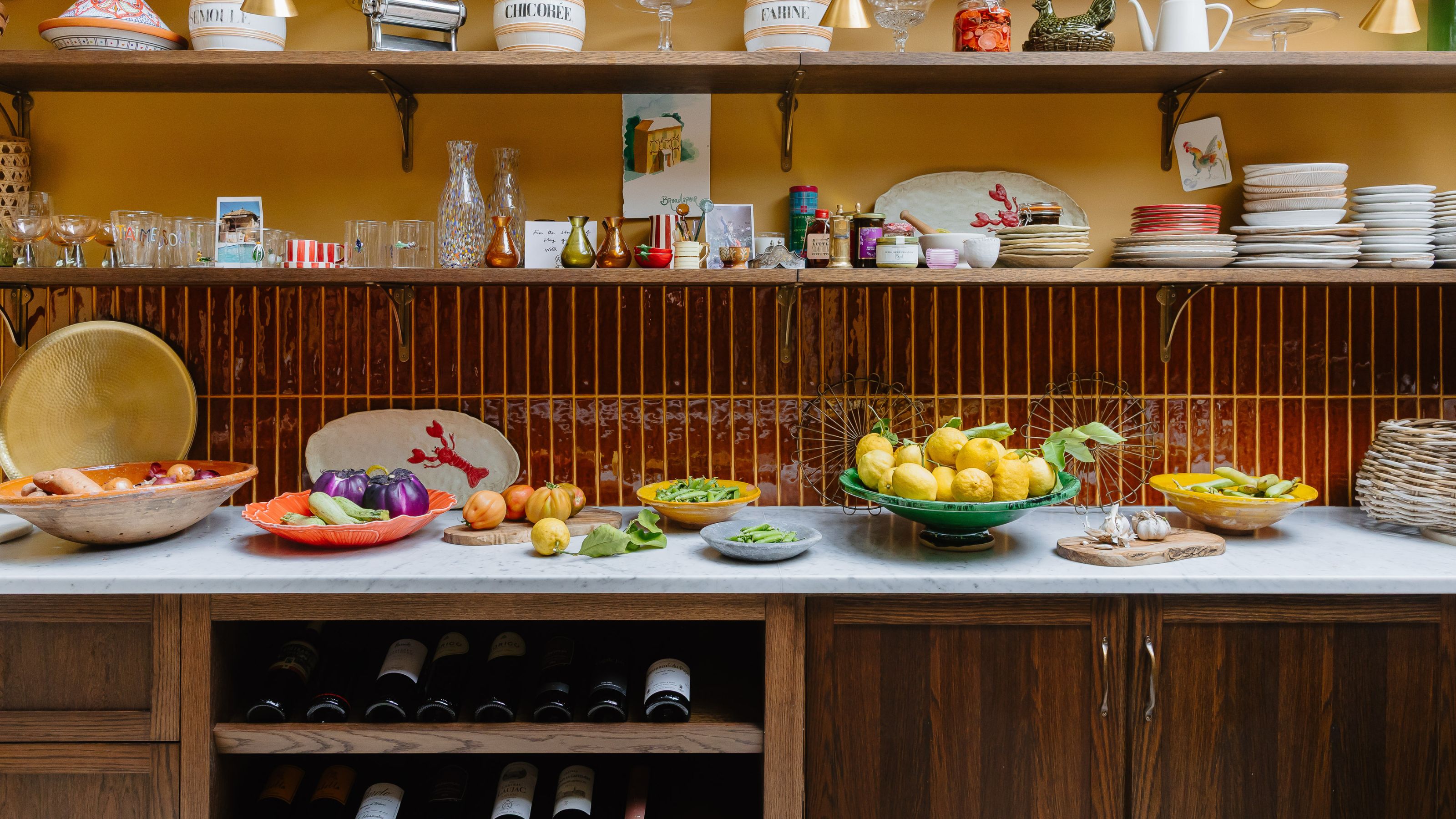 Clodagh McKenna's yellow and burgundy kitchen with open shelving, marble countertops, and wooden cabinetry including wine storage
