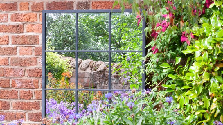 garden mirror against a brick wall and surrounded by planting
