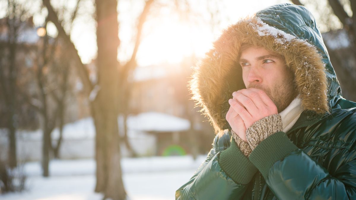 A man in the snow blows on his hands to stay warm