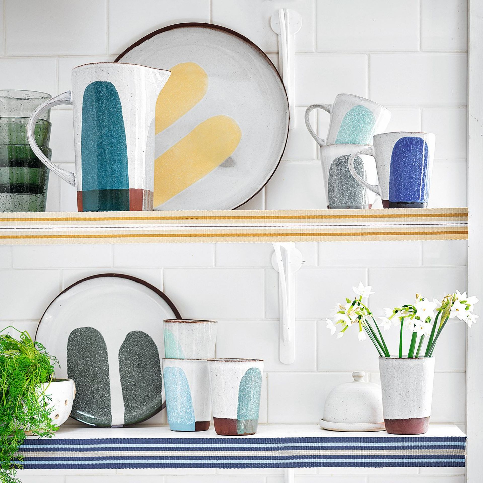 Kitchen worktop and shelves on white tiled walls with crockery and cheeseboard under glass dome