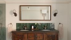 A vintage sideboard with a double basin green metro tiled splashback, large mirror above and side wall lamps
