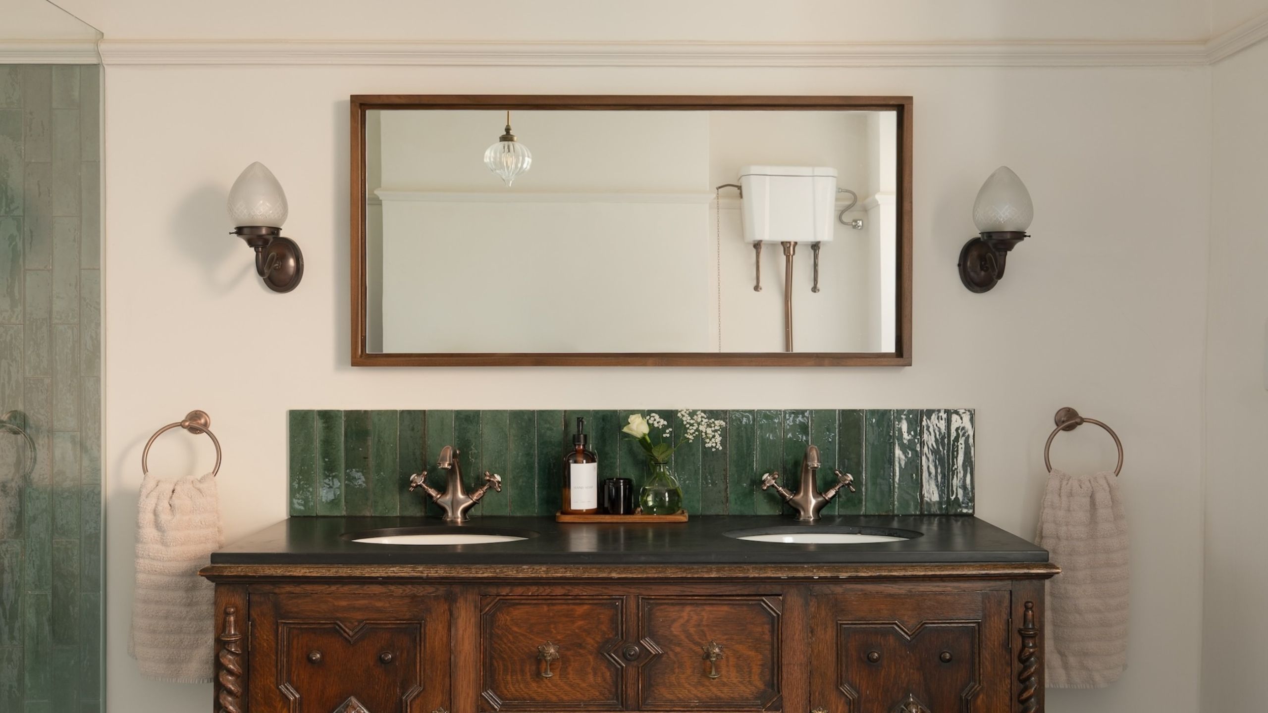 A vintage sideboard with a double basin green metro tiled splashback, large mirror above and side wall lamps