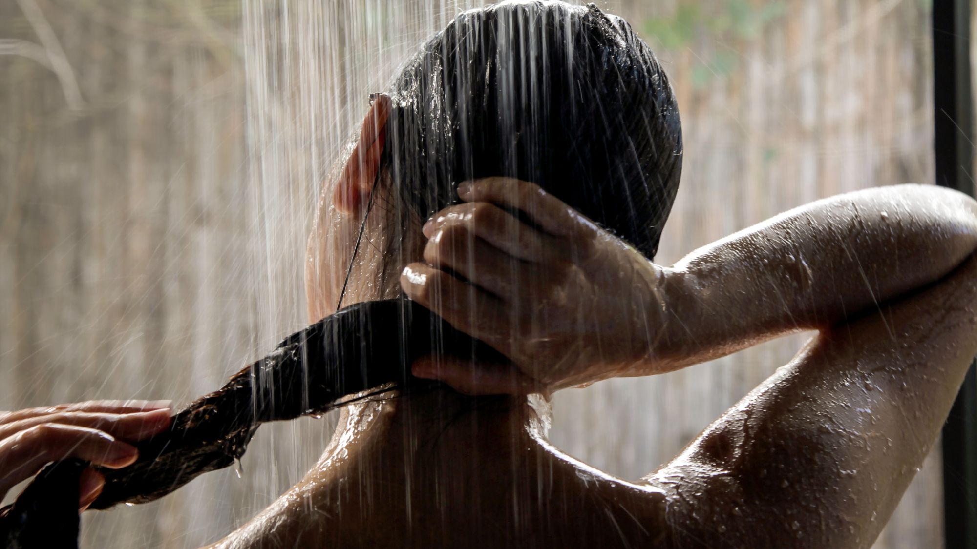 a close up of a woman from behind in the shower holding her hair
