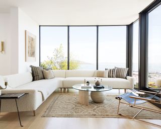 A minimalist living room with white walls and wrap around glass floor to ceiling windows