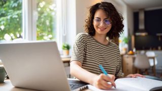 Woman researching on laptop with notebook and pen