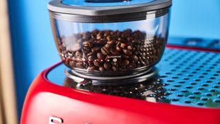 a red smeg espresso machine with burr grinder is photographed against a blue background