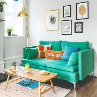 A small living room with a two-seater emerald green sofa against a white wall with contrasting cushions