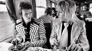 A photograph of Mick Ronson and David Bowie on a train eating lunch