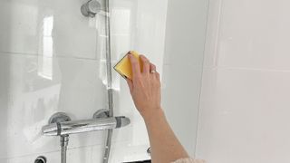 Glass shower door being scrubbed as a stage of how to clean a glass shower door