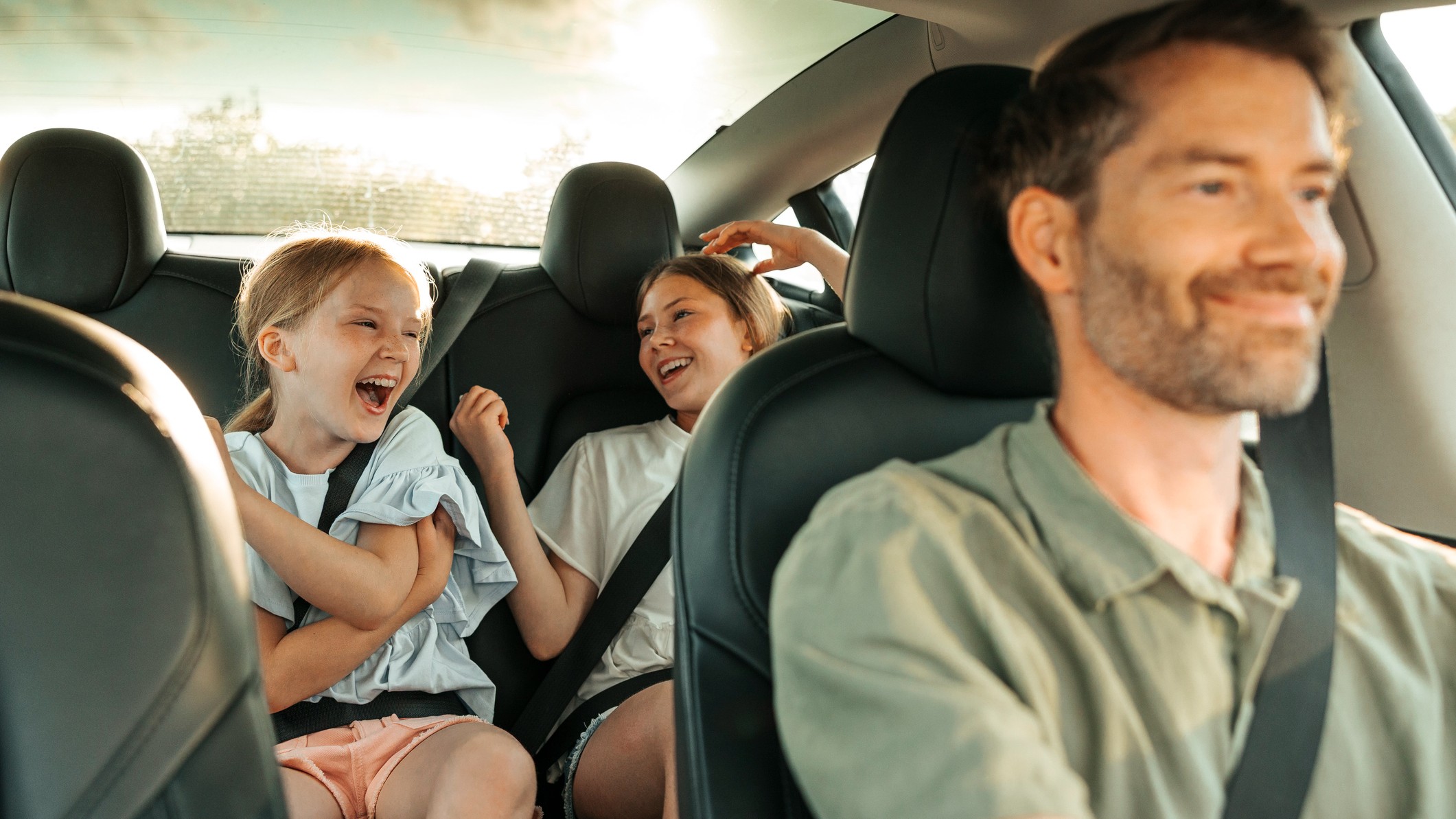 a happy dad driving while his daughters sit in the backseat telling jokes