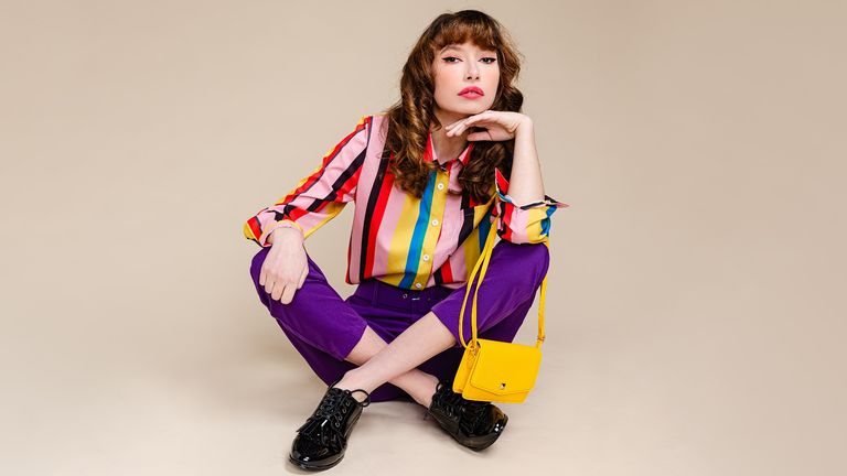 woman sitting wearing multi colored top and purple pants