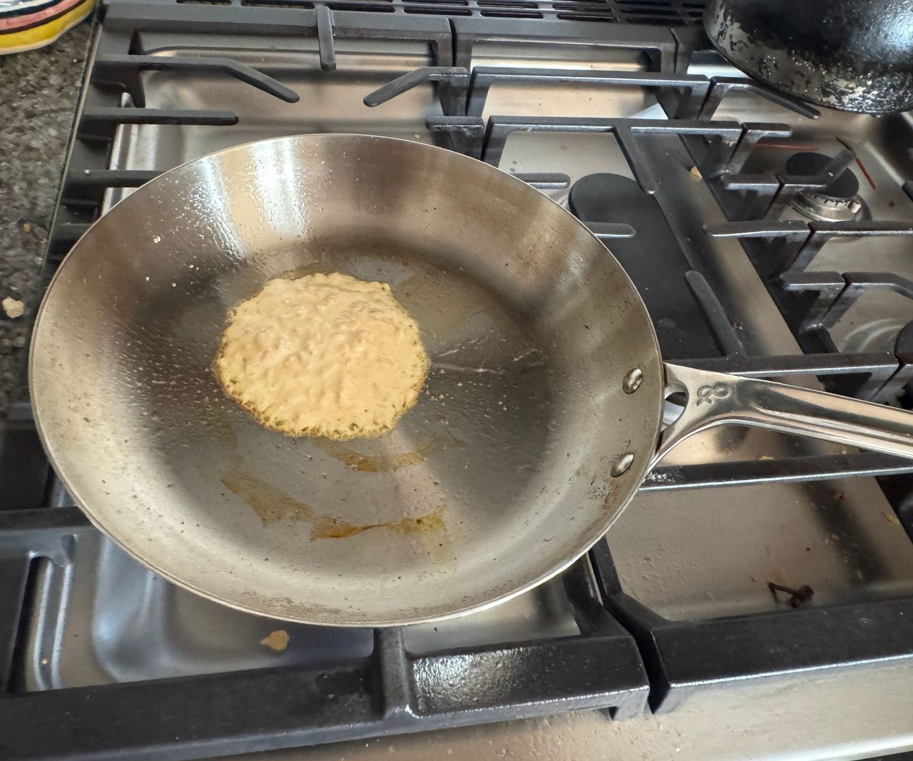 A stainless steel frying pan frying a single pancake on a gas stove