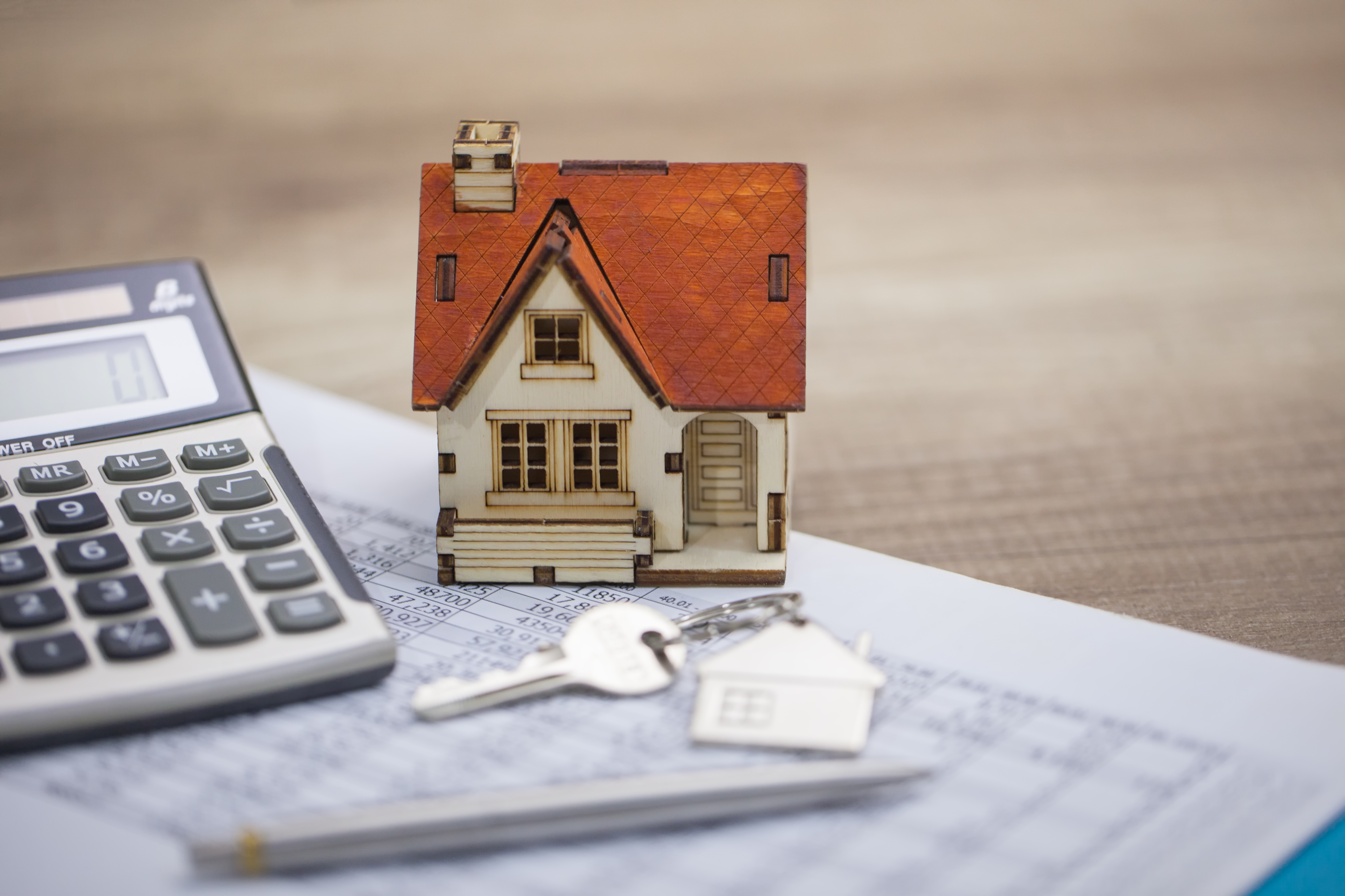 Model of property beside house key and calculator and financial documents