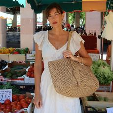 Woman wears white dress, raffia woven bag