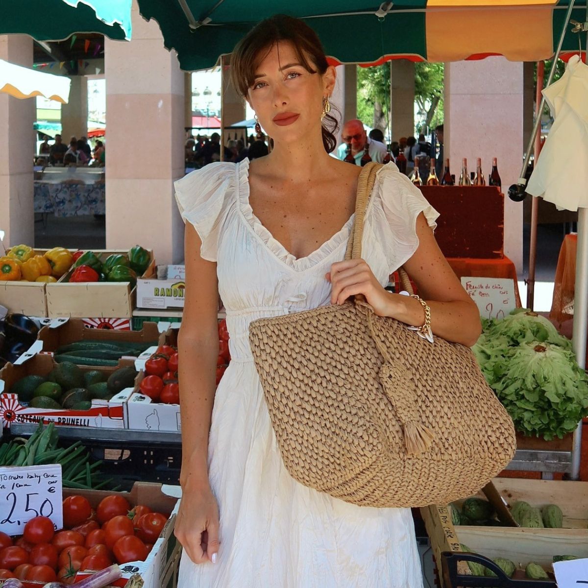 Woman wears white dress, raffia woven bag
