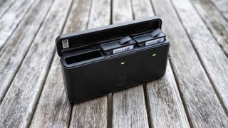 An open slim black case with two rectangular camera batteries inside on a faded wooden table.