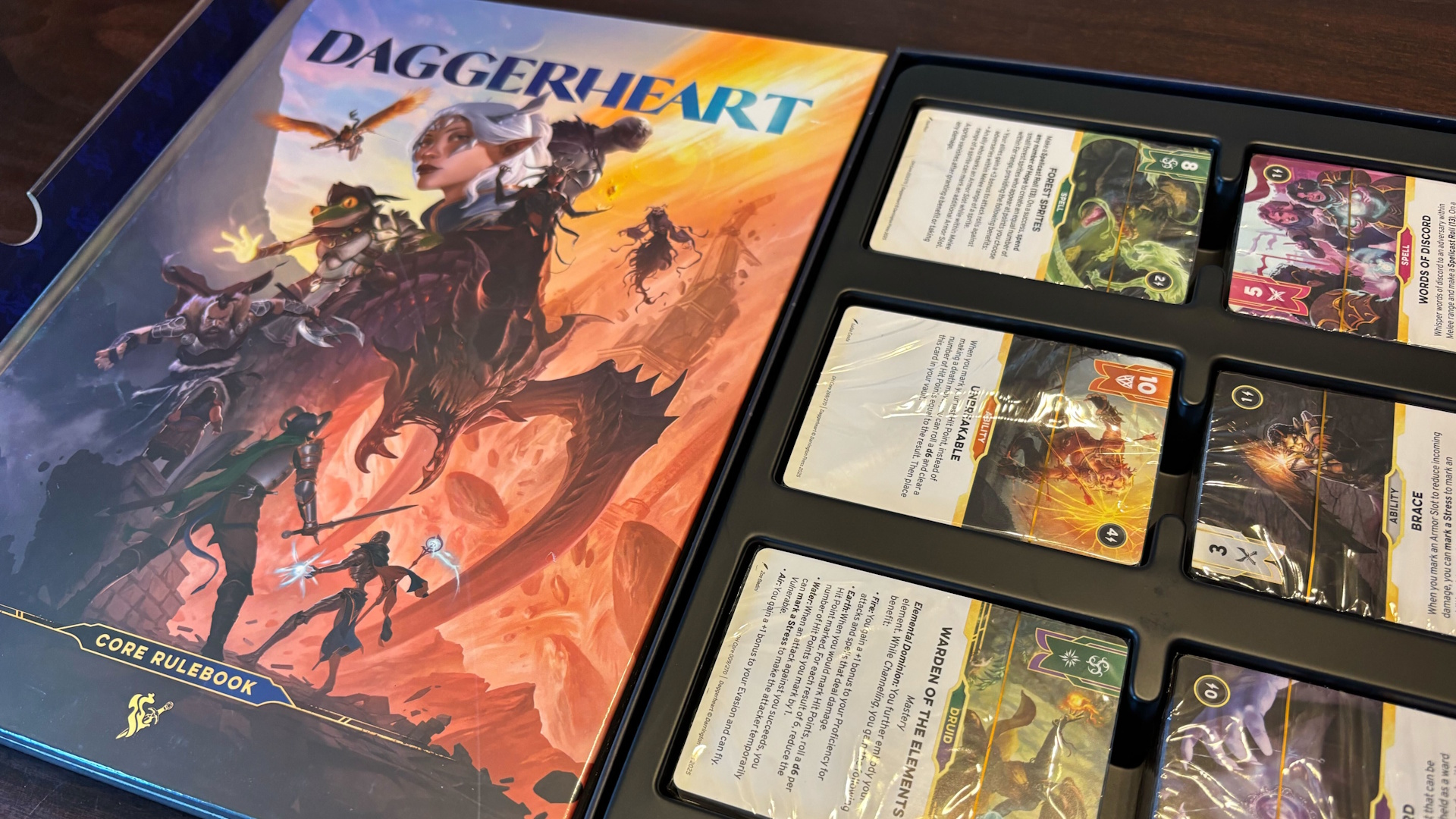 Photo of Daggerheart Core Set opened up to showcase the various decks next to the core rulebook