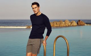 The CROSS Fine Egyptian Cotton Knitted Crewneck Sweater, ROSS Double Jersey Sweatshorts. A man standing with the sea behind him wearing casual clothing.