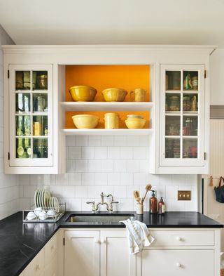 white kitchen with orange accent within open shelving, black marble countertop