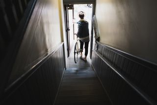 The best bicycle insurance should cover your bike when you leave home. This image shows someone exiting a front door with their bike at their side after carrying it down a flight of stairs