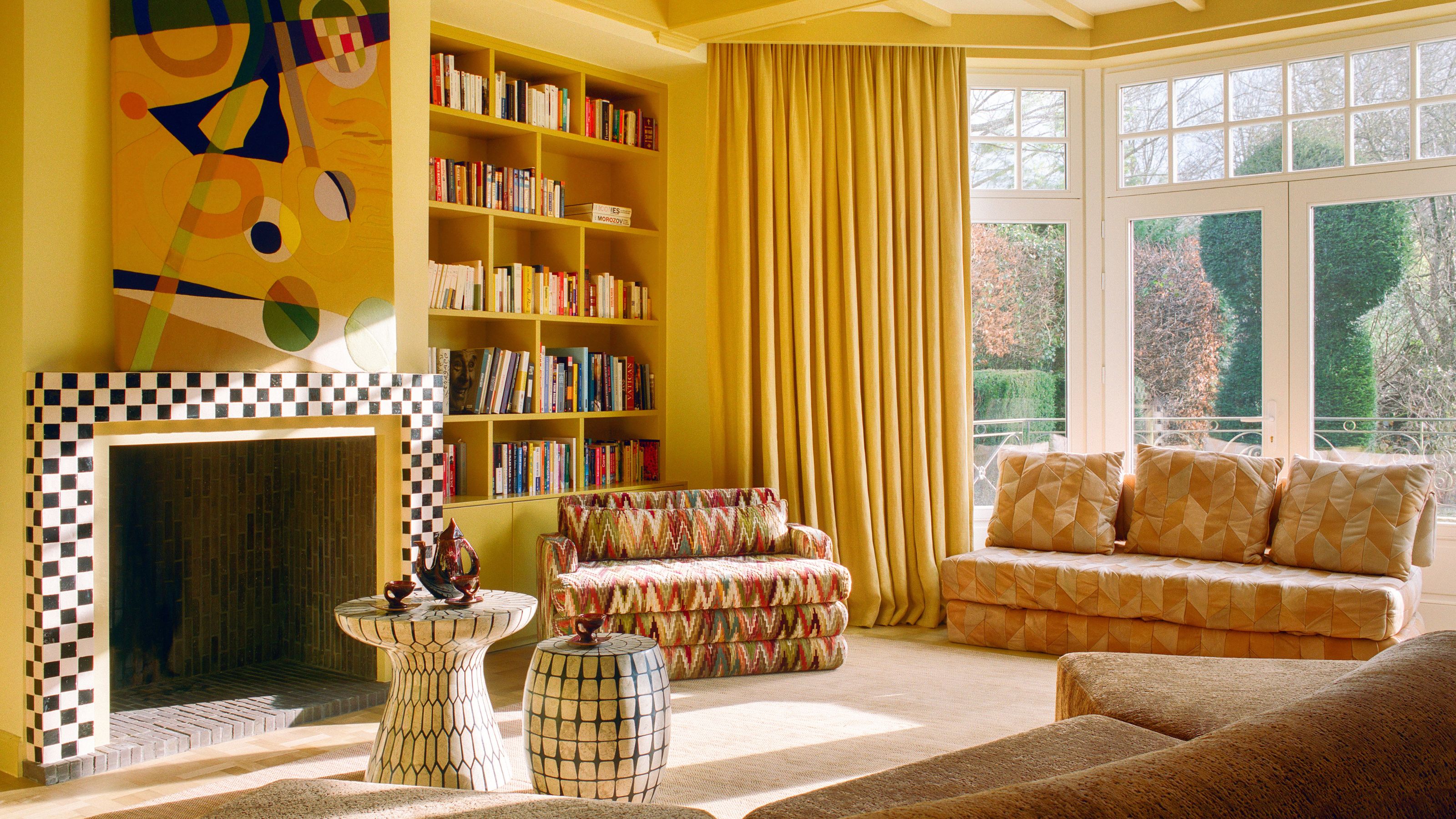 a bright yellow living room with bay window, checkerboard fire surround, eclectic art and bookcases